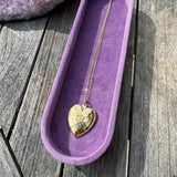 Necklace with a heart-shaped pendant in a purple case on a wooden surface