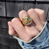 Hand wearing a gold horseshoe ring with intricate design on a wooden surface
