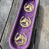 Three gold horseshoe necklaces in a purple display case on a wooden surface