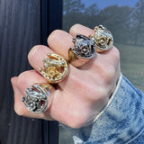 Hand wearing multiple horseshoe rings with intricate designs on a reflective surface.