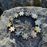 Decorative flower-shaped mother of pearl flowers bracelet arranged in a circular pattern on a textured stone surface.