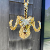 Gold ram head pendant on a chain against a reflective surface