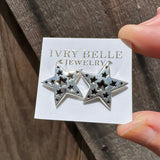 Silver star-shaped jewelry on a card with 'Ivy Belle Jewelry' branding, held over a wooden surface.