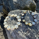 Floral shapes in white and blackened chatoyance mother of pearl bracelets resting upon a textured beach rock 