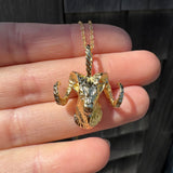 Gold ram head pendant held in a hand ring with a blurred background