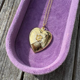 Gold heart-shaped pendant on a chain in a purple jewelry box on a wooden surface