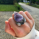 Hand wearing a silver ring with a purple stone outdoors