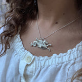 Close-up of a girl with curly hair wearing a silver  hippocampus necklace in a white blouse.