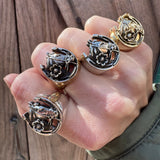Hand wearing multiple horseshoe rings on against a wooden backdrop.