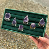 Set of purple and silver rings in a green display box held by a hand on a gravel surface.