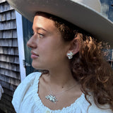 A girl wearing a white blouse in a beige cowboy hat, with close-up of jewelry. She is wearing a sterling silver hippocampus pendant and earrings in sterling silver.