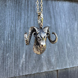 Bronze ram head pendant on a chain against a wooden background