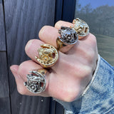 Hand wearing multiple horseshoe rings on against a wooden backdrop.