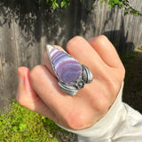 Hand wearing a large purple stone ring with silver band outdoors.