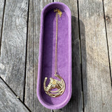 Velvet purple jewelry dish with a gold necklace on a wooden surface