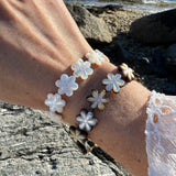 Close-up of a wrist wearing a bracelet with white flower-shaped charms against a natural background.