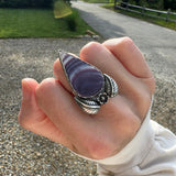 Hand wearing a silver ring with leaves and a flower with a tear drop shaped quahog shell.