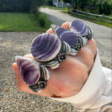 Hand waring four large quahog shell rings that are purple and white with floral accents against a natural background