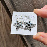 Star-shaped silver earrings on a 'Ivy Belle Jewelry' card held by a hand on a wooden surface.