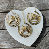 Three gold horse head and horseshoe necklaces on a heart-shaped white stone with wooden background