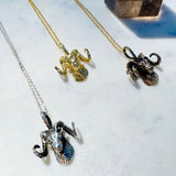 Three ram head necklaces in gold, silver, and bronze on a white surface with a crystal in the background.