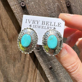 Turquoise stone earrings held by a hand on a wooden surface with 'Ivory Belle Jewelry' card.