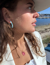 Woman wearing a white hat and earrings, with a scenic background of water and buildings.