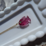 Pink fish-shaped pendant on a gold chain against a white decorative background