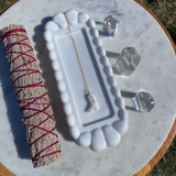 White foot-shaped dish with a necklace, crystal, and sage on a marble surface.