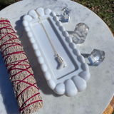Jewelry dish with necklace, crystal, and sage on a marble surface outdoors