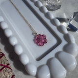 Necklace with a pink flower pendant on a white dish, surrounded by crystals.