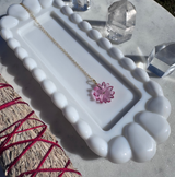 White jewelry dish with a necklace featuring a pink flower pendant on a marble surface with crystals.
