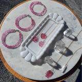 Jewelry set including pink beaded bracelets, earrings, and crystals on a marble surface.