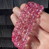 Hand holding a pink beaded bracelet against a dark background