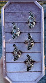 Five silver and bronze floral rings with blackened daisy flowers on a pink ring tray.