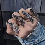 Hand wearing multiple silver floral rings against a wooden background