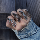 Hand wearing multiple floral silver rings against a wooden background