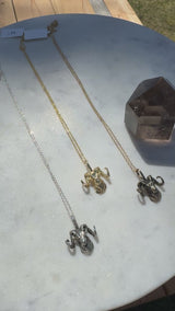 Three ram head necklaces in sterling silver, gold plate, and bronze on a white marble background and smoky quartz crystal.