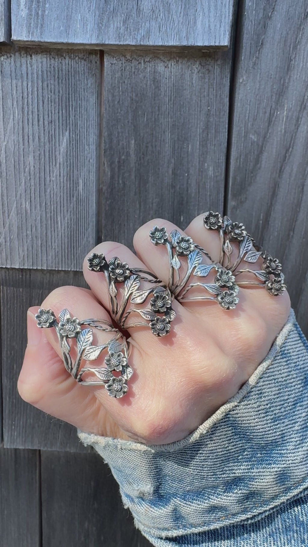 Hand wearing multiple floral silver rings against a wooden background.